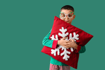 Cute little boy in Christmas eyeglasses with pillow on green background