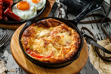 Delicious breakfast, omelette with vegetables and cheese served on hot pan over wooden background. Healthy food breakfast, close up