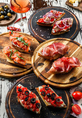 Variety of bruschetta with prosciutto, tuna, salmon, grilled pepper, tomatoes, cheese, sauce, olives on ciabatta bread on wooden board over rustic background. Sandwiches set of wine, top view - obrazy, fototapety, plakaty