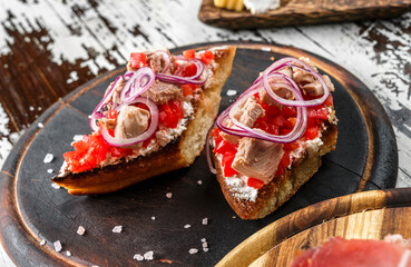 Bruschetta with tuna fish, bell pepper, cream cheese and onion on ciabatta bread on wooden board over rustic background. Healthy food, sandwich of wine, close up