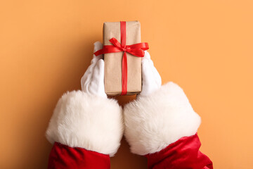 Santa hands with gift box on color background, closeup
