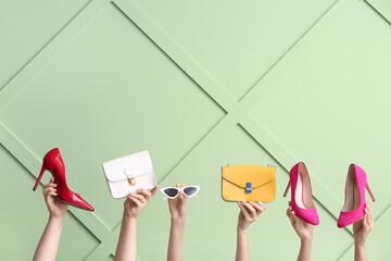 Female hands with stylish high heels, handbags and sunglasses against color wall