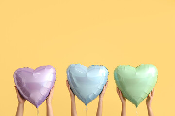 Female hands with heart shaped foil balloons on color background