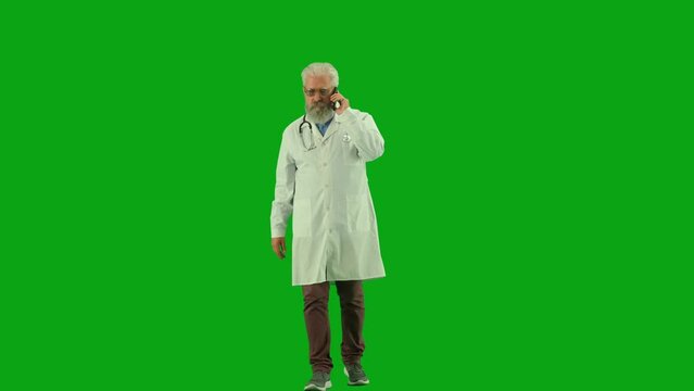 Portrait of aged man medic on chroma key green screen. Senior doctor in uniform walking and talking answering call on smartphone.