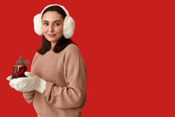 Beautiful young woman in warm mittens with glass of hot mulled wine on red background