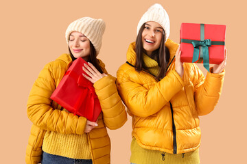 Young women in winter clothes with Christmas gifts on beige background