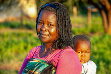 village african mother with braids carry child in the back wrapped in a blanket