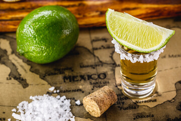 glasses of golden tequila, served with salt and lemon, over vintage map of mexico