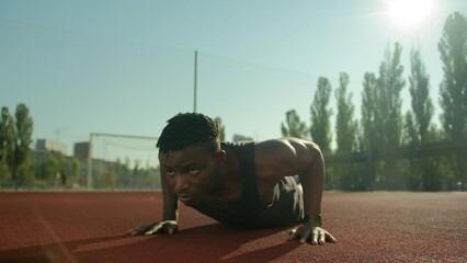 Motivated African American sport man athlete bodybuilder doing push ups exercise on football stadium male young sportsman fitness trainer in city training arms biceps muscles summer workout outdoors - Powered by Adobe