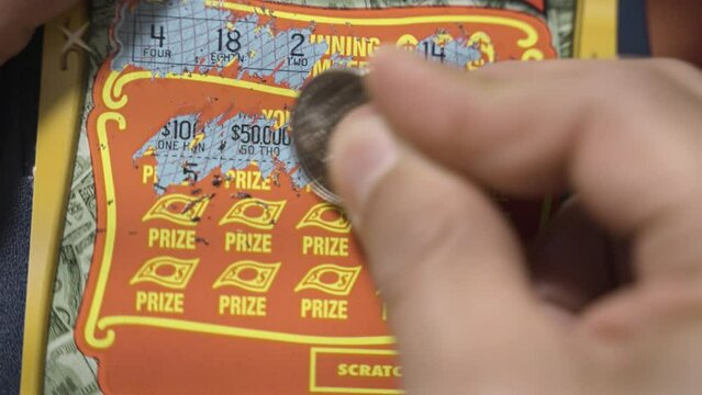 Close up of a male hand using a coin to scratch numbers on a lottery card.