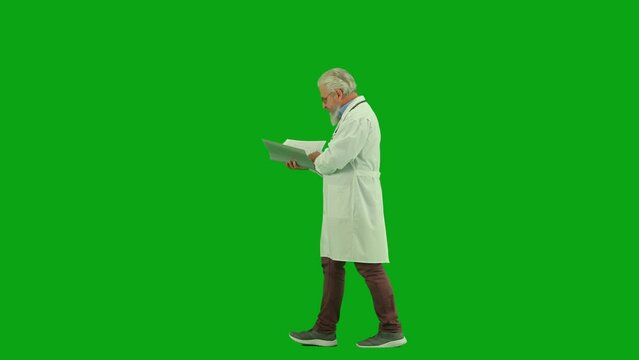 Portrait of aged man medic on chroma key green screen. Side view senior doctor walking through clinic or hospital with paper medical card.