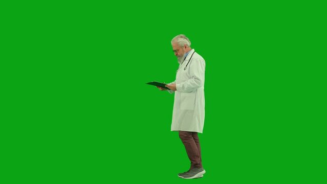 Portrait of aged man medic on chroma key green screen. Side view senior doctor walking in clinic or hospital with clipboard and writing in it.
