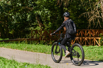 Obraz na płótnie Canvas In the radiant embrace of a sunny day, a modern woman revels in the joy of cycling, her sleek bicycle and professional gear complementing her active lifestyle as she rides through the park