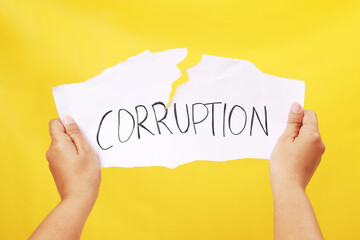 Stop and fight corruption concept. Human hand tearing a piece paper with written word corruption. Isolated on yellow background