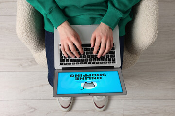 Man using laptop for online shopping in armchair indoors, top view