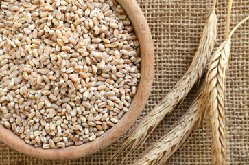 Wheat groats in a wooden bowl with ears on burlap on a wooden background. Rustic style. Concept of healthy food. Horizontal orientation. Selective focus. Top view