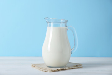 Jug of fresh milk on white wooden table against light blue background