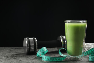 Tasty shake, dumbbell and measuring tape on grey table against black background, space for text....