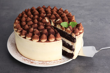Delicious tiramisu cake with mint leaves and server on grey table