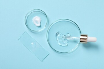 Fototapeta premium Petri dishes with samples of cosmetic serums and pipette on light blue background, flat lay