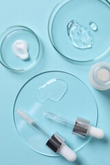 Petri dishes with samples of cosmetic serums, bottle and pipettes on light blue background, flat lay