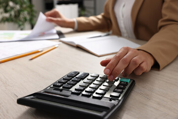 Woman using calculator while working with document at wooden table, closeup