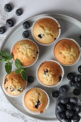 Delicious sweet muffins with blueberries and mint on white marble table, flat lay