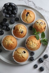 Delicious sweet muffins with blueberries and mint on white marble table, flat lay