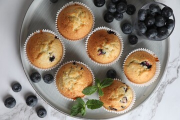 Delicious sweet muffins with blueberries and mint on white marble table, flat lay