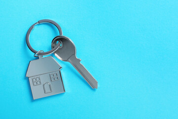Key with keychain in shape of house on light blue background, top view. Space for text