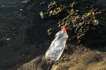 Used plastic bottle near water at beach, top view and space for text. Environment pollution