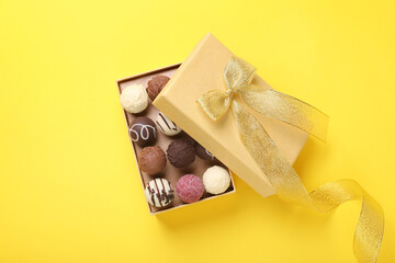 Open box with delicious chocolate candies on yellow background, top view