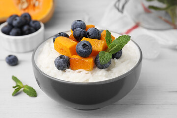 Bowl of delicious rice porridge with blueberries, pumpkin and mint on white table, closeup