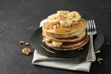 Delicious pancakes with bananas, walnuts and honey on dark textured table, closeup. Space for text
