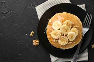 Delicious pancakes with bananas, walnuts and honey on dark textured table, top view. Space for text