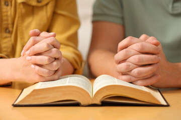 Family couple praying over Bible together at table indoors, closeup