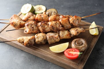 Delicious shish kebabs with vegetables and lemon on grey table