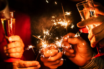 close up of sparklers and glass of champagne together celebrating the new year or the christmas day or another party together - people having fun