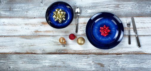Holiday dinner table setting of an empty main dark blue dish and bowl with Christmas or New Years decorations plus cutlery on rustic white wood