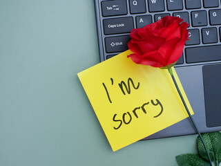 Top view of words i'm sorry written on sticky note on laptop keyboard with roses