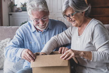 Happy mature aged older family couple unpacking carton box, satisfied with internet store purchase...