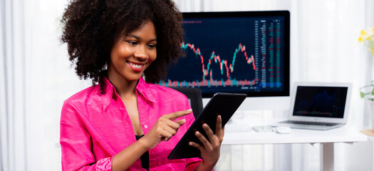 Analytical young African American businesswoman, a specialist in successful stock exchange trading, against dynamic data graph displaying marketing trend analysis on screen. Tastemaker. - obrazy, fototapety, plakaty