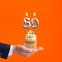 The hand that delivers cupcake with the number 50 candle - Birthday on orange background