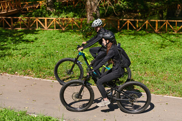 Naklejka premium A blissful couple, adorned in professional cycling gear, enjoys a romantic bicycle ride through a park, surrounded by modern natural attractions, radiating love and happiness