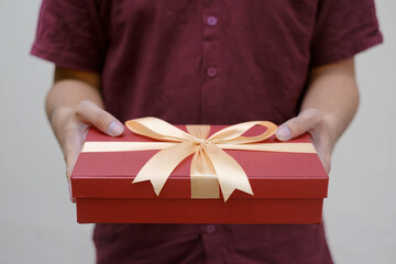 Male hands holding a small red gift box wrapped with gold ribbon. Close up and indoor shot....