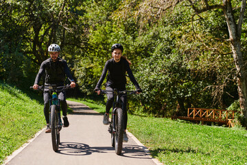 Obraz premium A blissful couple, adorned in professional cycling gear, enjoys a romantic bicycle ride through a park, surrounded by modern natural attractions, radiating love and happiness