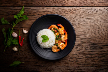 Stir-fried shrimp with basil Thai street food arranged on a black plate Spicy Thai food placed on a wooden table. Top view.