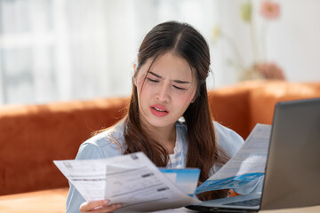 Young Asian woman looks stressed while examining a bill, impactful financial pressure, anxiety, and the challenges of managing expenses. Financial problem.