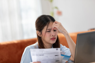 Young Asian woman looks stressed while examining a bill, impactful financial pressure, anxiety, and...