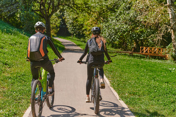Naklejka premium A blissful couple, adorned in professional cycling gear, enjoys a romantic bicycle ride through a park, surrounded by modern natural attractions, radiating love and happiness